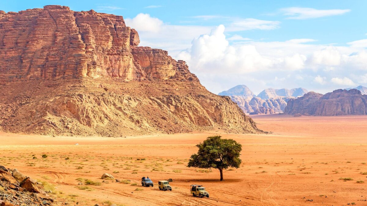 4x4 jeep driving across red sand dunes among towering rock formations in Wadi Rum desert