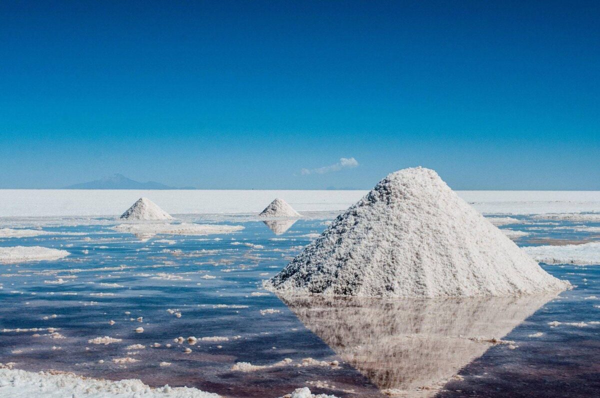 4x4 vehicle driving across the blinding white Uyuni Salt Flats with a cactus-covered island rising in the background