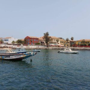 A traditional motorized pirogue gliding through a Senegalese river lined with lush mangrove trees under a bright blue sky