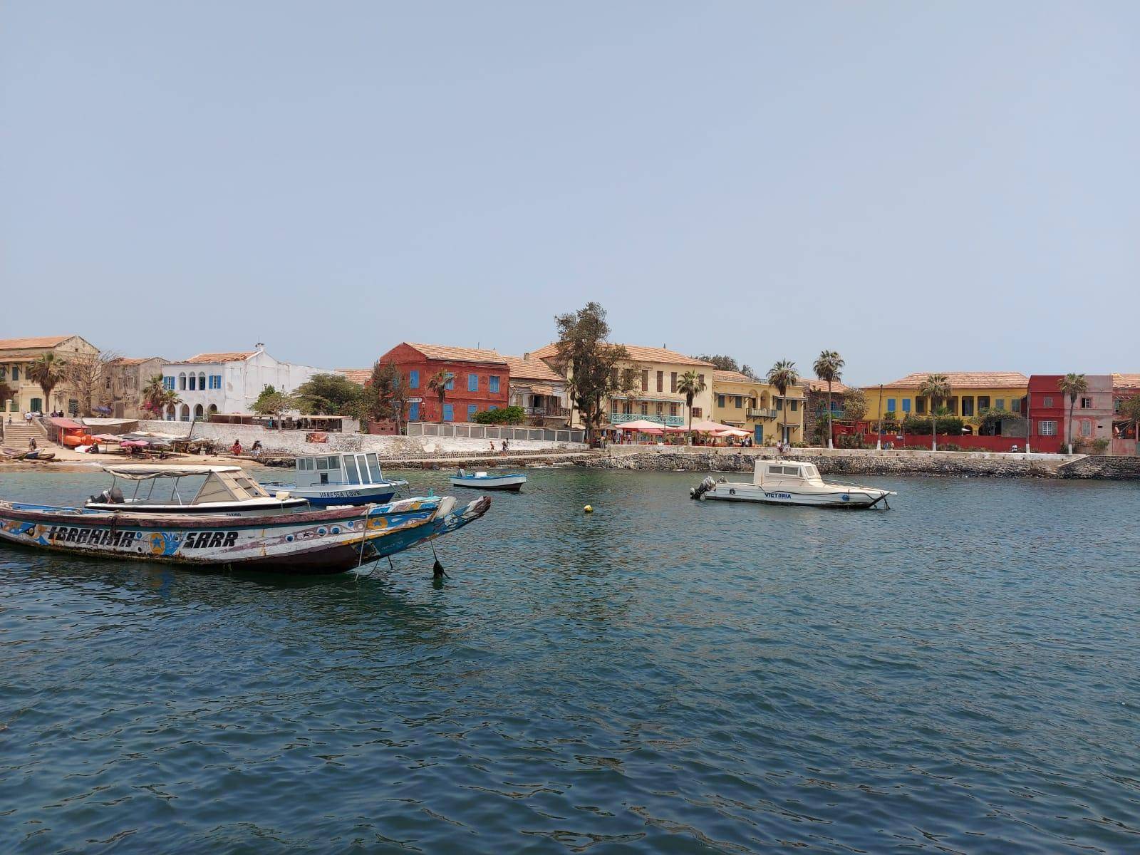 A traditional motorized pirogue gliding through a Senegalese river lined with lush mangrove trees under a bright blue sky