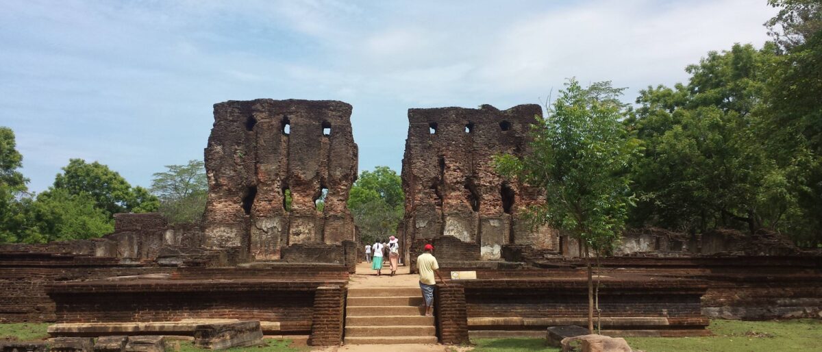 Ancient stone stupas and Buddha statues among green lawns and trees at the archaeological site of Polonnaruwa in Sri Lanka