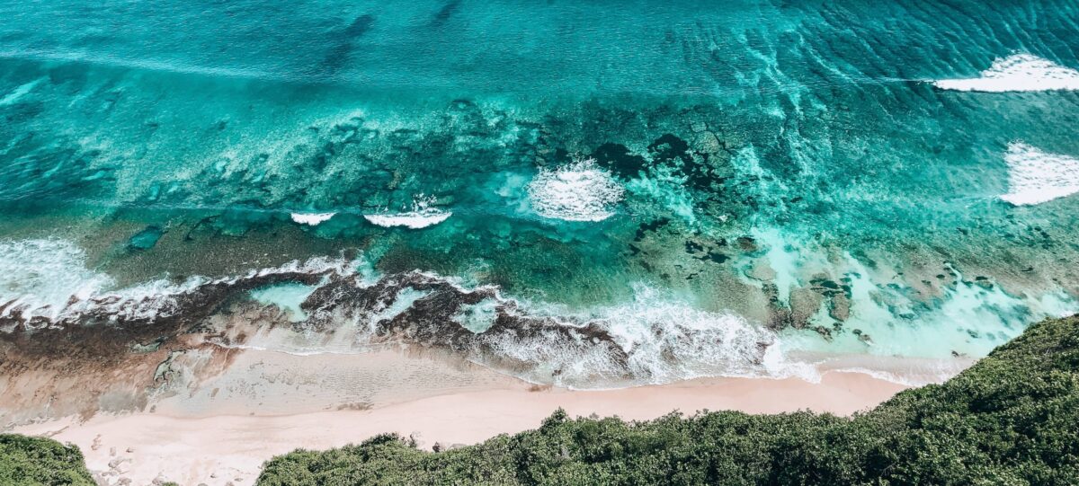 Balangan Beach with golden sand, reef breaks and surfers in the waves below limestone cliffs