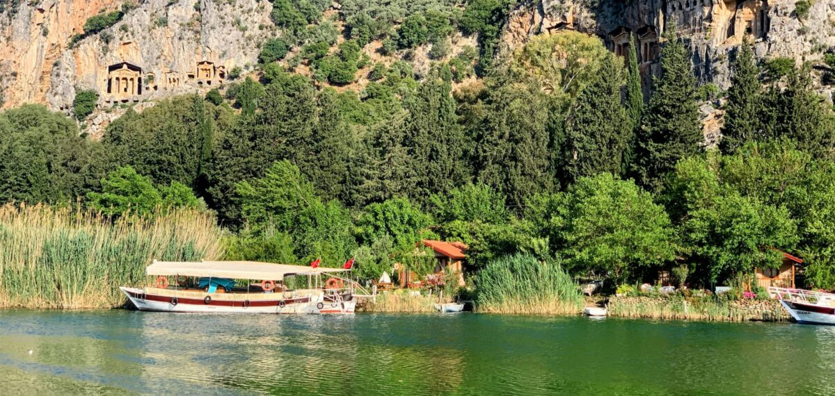 Boat cruising on the Dalyan River with Lycian rock tombs carved into cliffs in the background