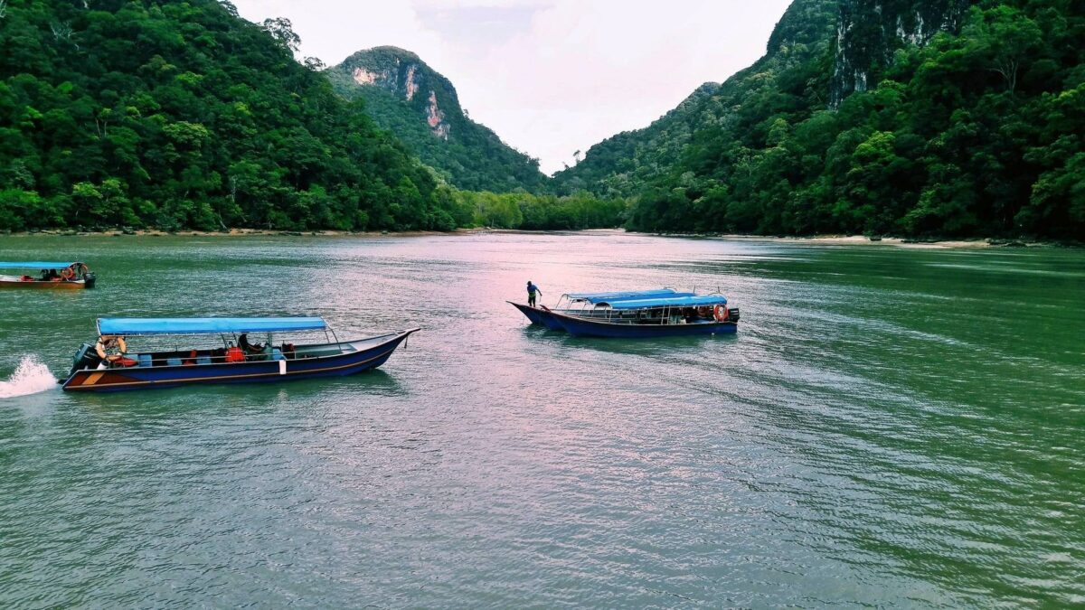 Boat navigating between limestone cliffs and dense mangrove forest in Langkawi