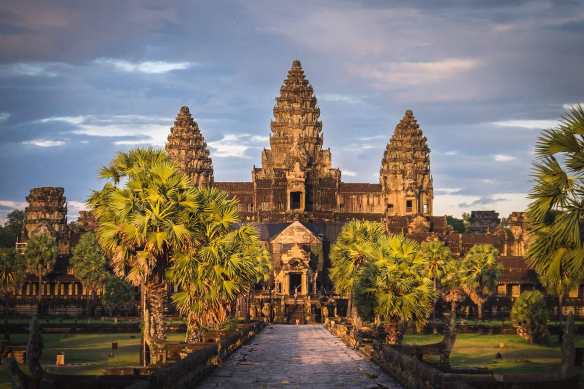 Busy street in Siem Reap with tuk-tuks, shops and palm trees near sunset