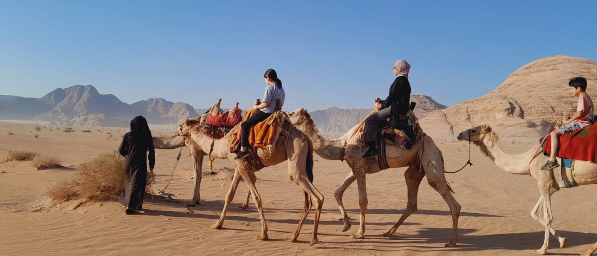Camels carrying a family across the red sand dunes of Wadi Rum at sunset