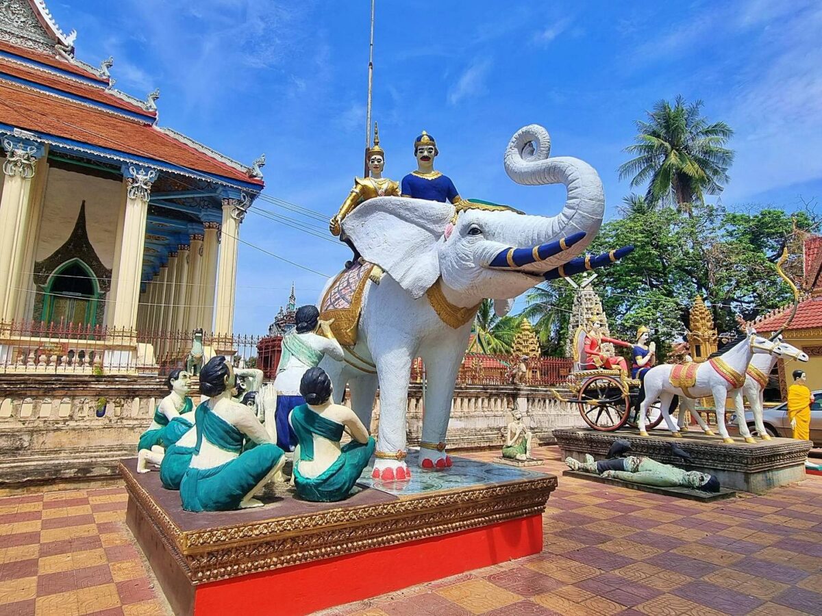 Cyclists riding along a rural path past rice fields near Battambang and traditional boats on the Sangke River