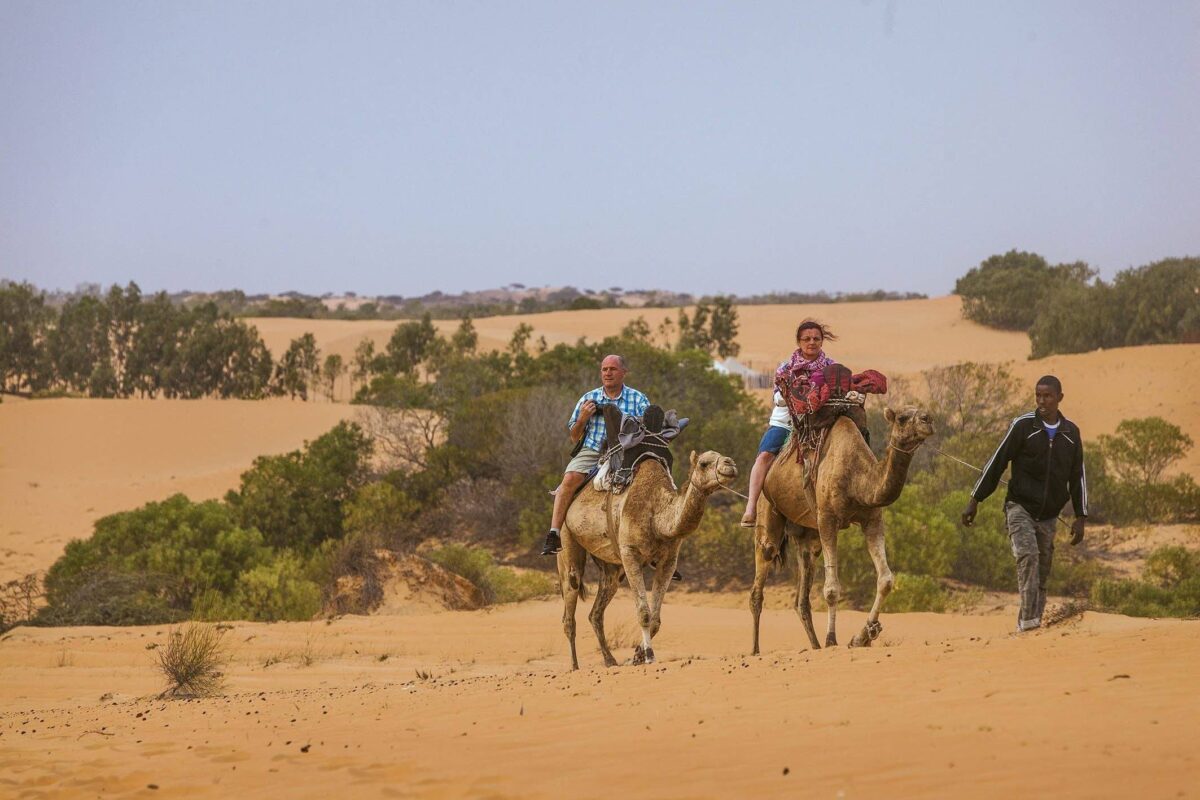 Desert camp set among the orange dunes of Lompoul at sunset with traditional tents and a 4x4 parked nearby