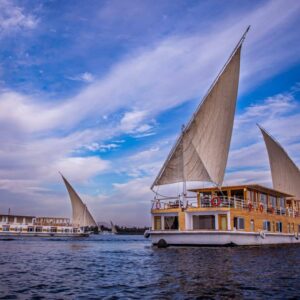 Elegant Dahabiya sailing on the Nile at sunset with ancient Egyptian temples and desert hills in the background