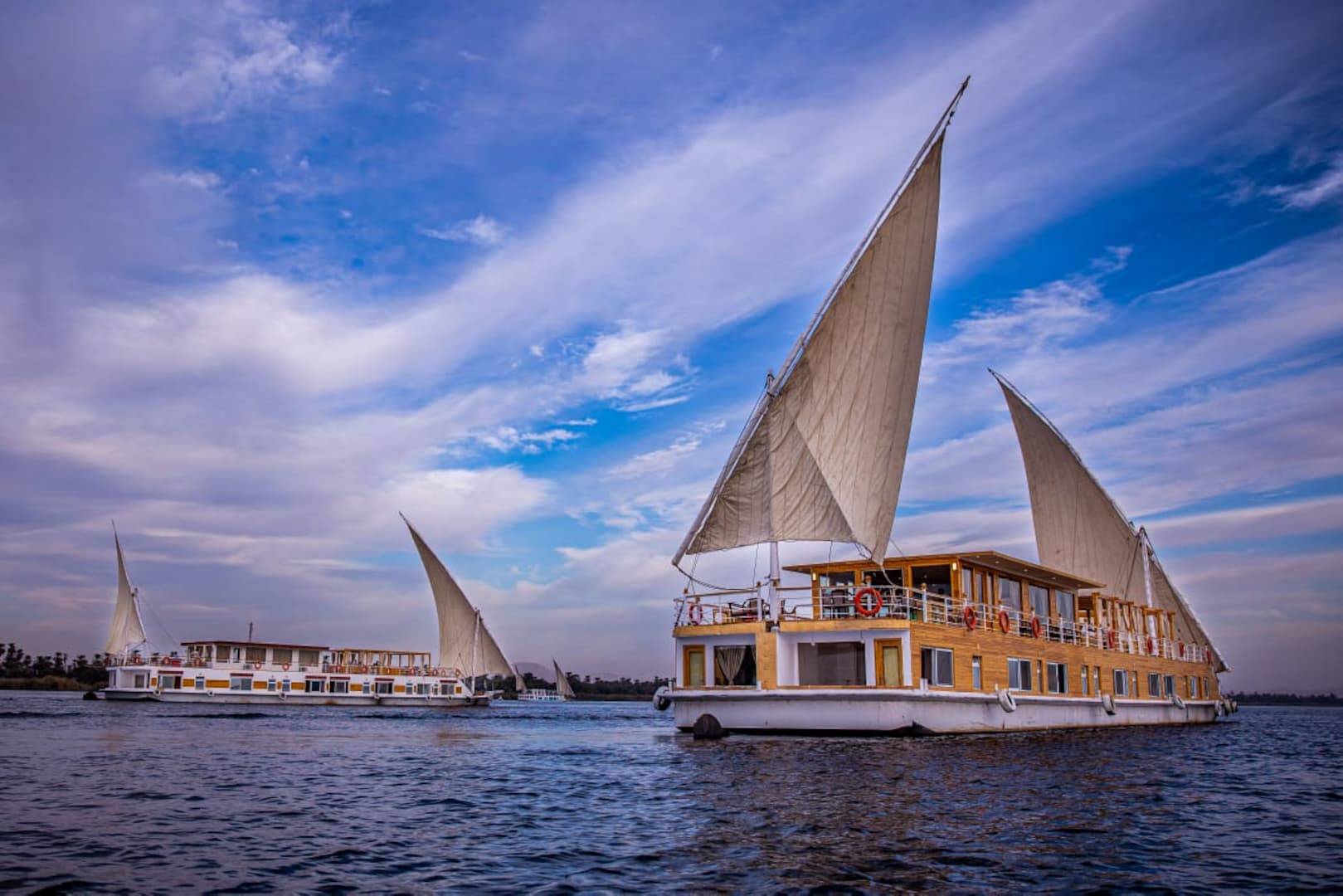 Elegant Dahabiya sailing on the Nile at sunset with ancient Egyptian temples and desert hills in the background