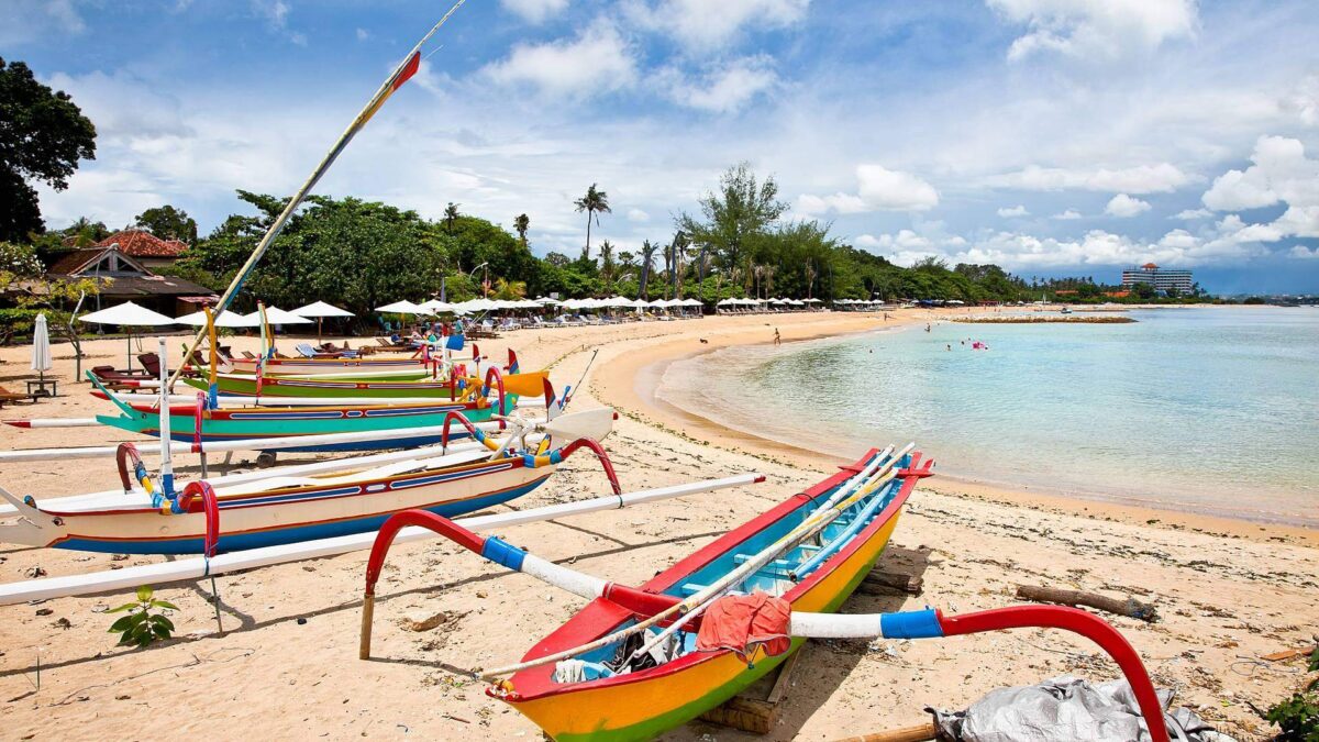Family playing on the sandy beach of Sanur with calm sea and traditional boats in the background