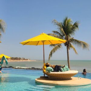 Family walking along a quiet sandy beach in Somone, Senegal, with palm trees, calm waves and a relaxed seaside hotel in the background