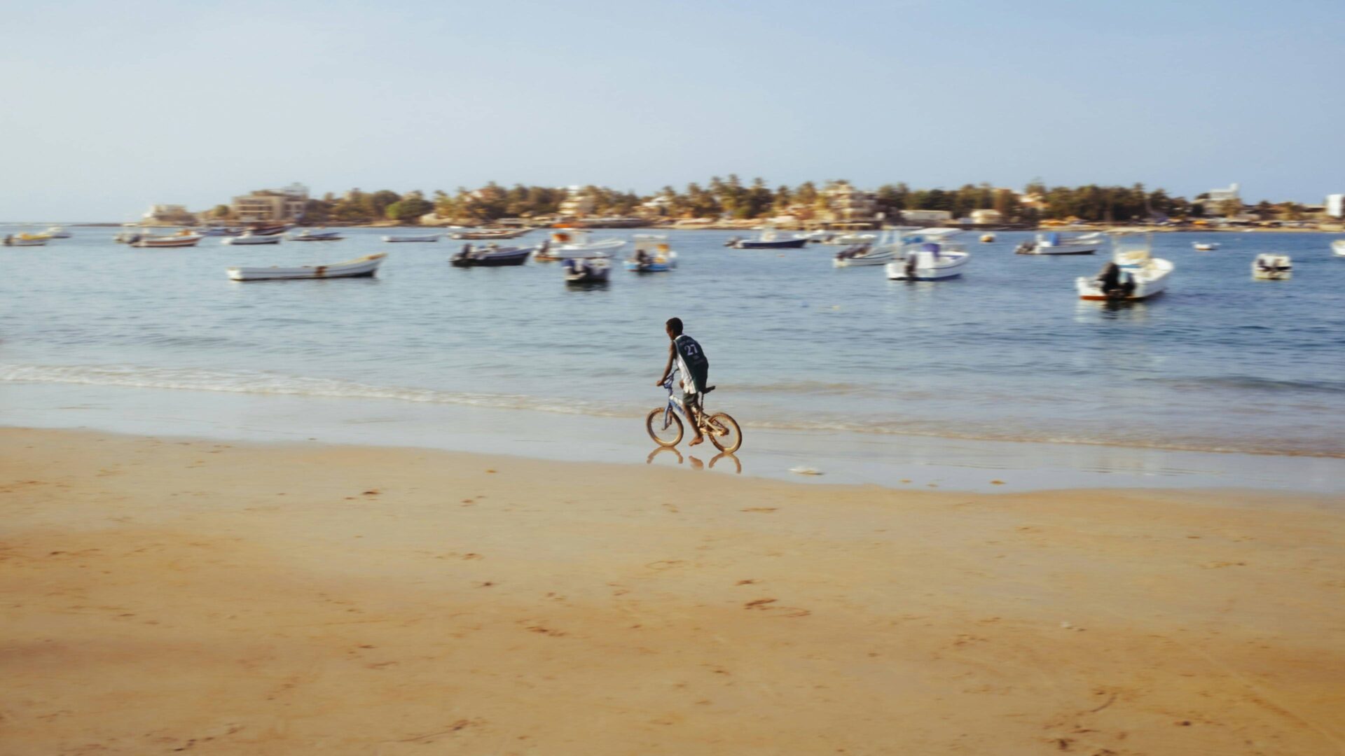 Family walking along the pink waters of Lake Retba in Senegal with traditional pirogues and sand dunes in the background