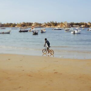 Family walking along the pink waters of Lake Retba in Senegal with traditional pirogues and sand dunes in the background