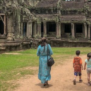 Family with young children riding in a tuk-tuk near ancient Angkor temple ruins surrounded by jungle in Cambodia at sunset