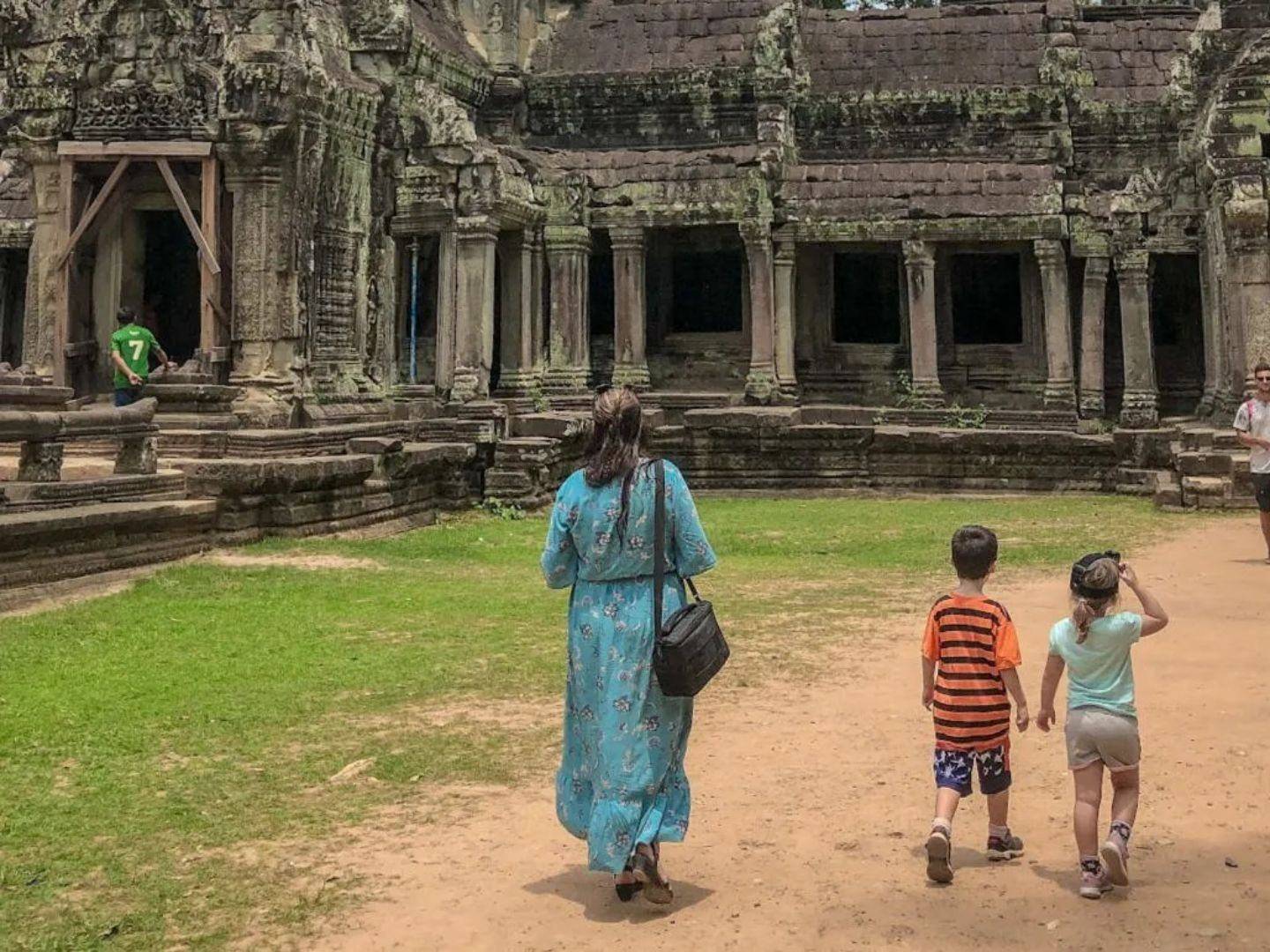 Family with young children riding in a tuk-tuk near ancient Angkor temple ruins surrounded by jungle in Cambodia at sunset