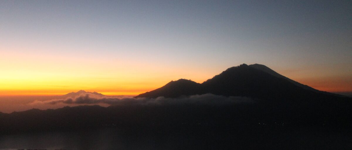 Hikers watching sunrise from the summit of Mount Batur with clouds and Lake Batur below