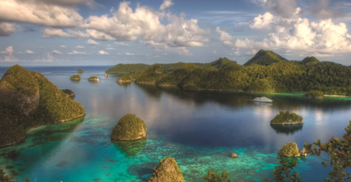 Idyllic Raja Ampat beach with white sand, clear turquoise water and jungle-covered islets in the background