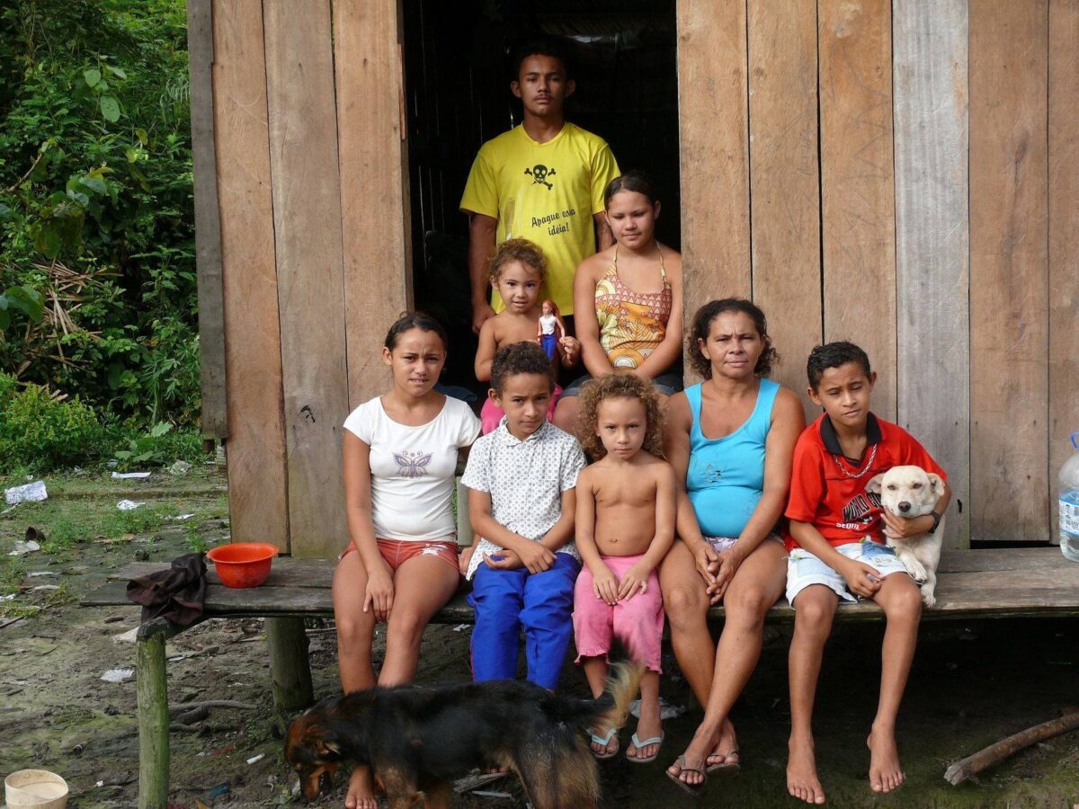 Indigenous wooden houses on stilts along an Amazon riverbank with a canoe and dense jungle in the background