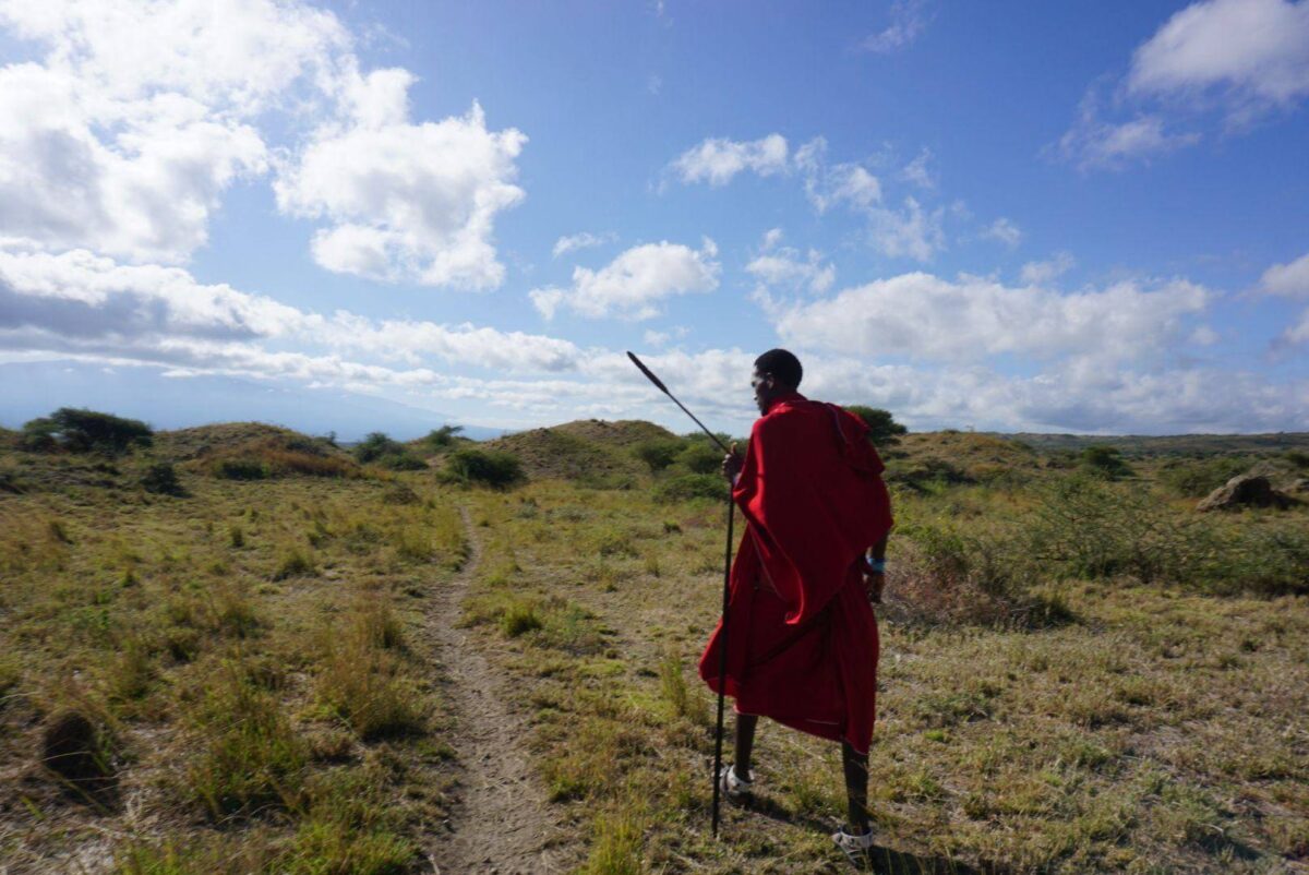 Maasai guide walking with a family near traditional huts with Mount Kilimanjaro in the distance