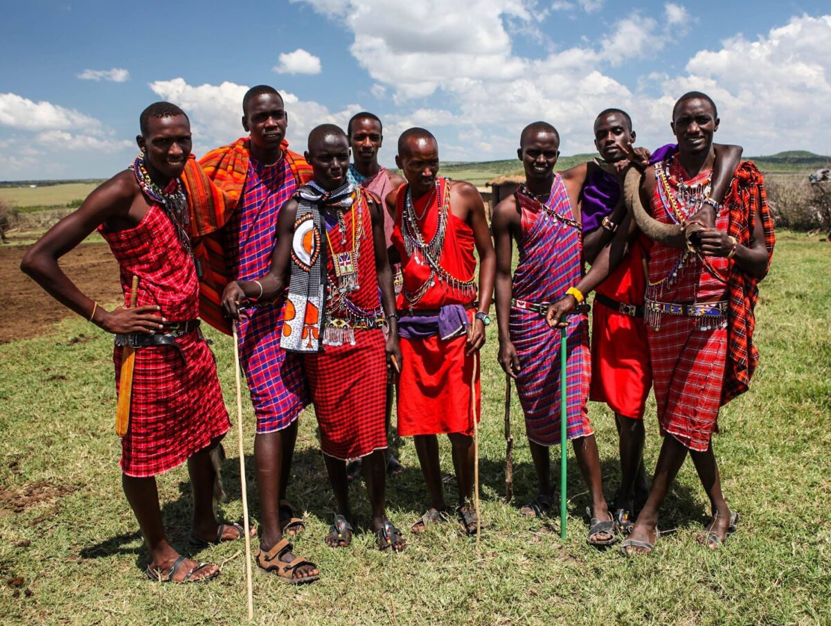 Masai men in traditional red shuka garments standing on a grassy hill with wide savanna views