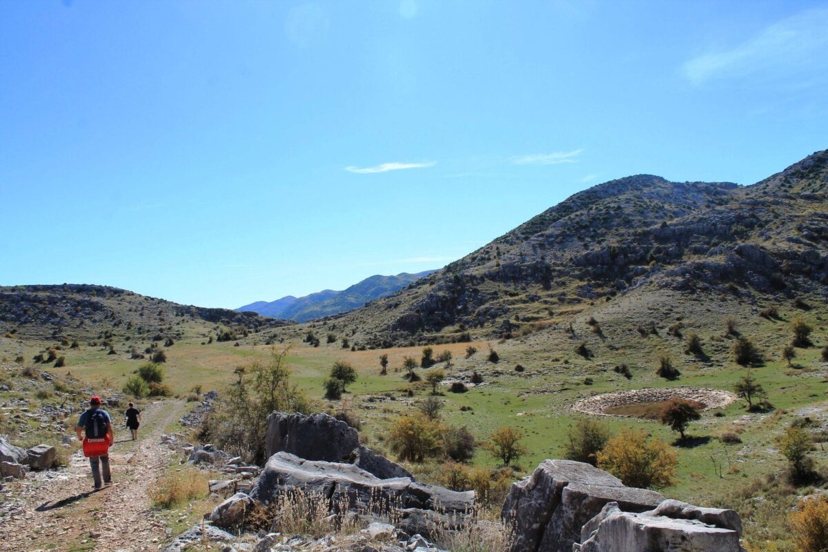 Mountain hikers walking along a rocky trail near a high pass with pine trees in southern Albania