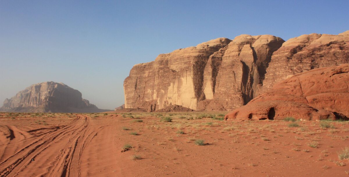 Off-road jeep and camels crossing the red sand dunes and rock formations of Wadi Rum desert