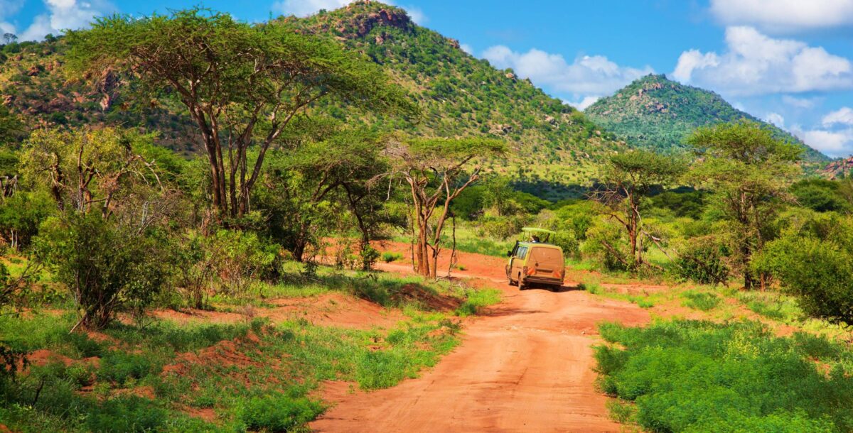Open savanna landscape in Tsavo East National Park with red soil, scattered bushes and distant hills