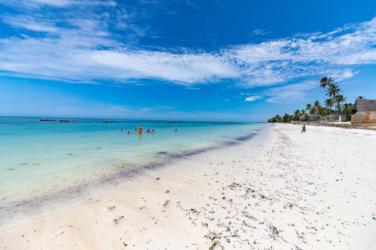 Palm-fringed beach in Zanzibar with white sand, turquoise water and families relaxing by the shore