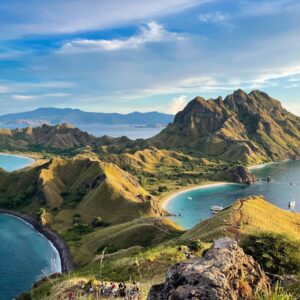 Panoramic view of a Balinese coastal temple on a rocky outcrop at sunset with waves crashing against the cliffs and lush greenery in the background