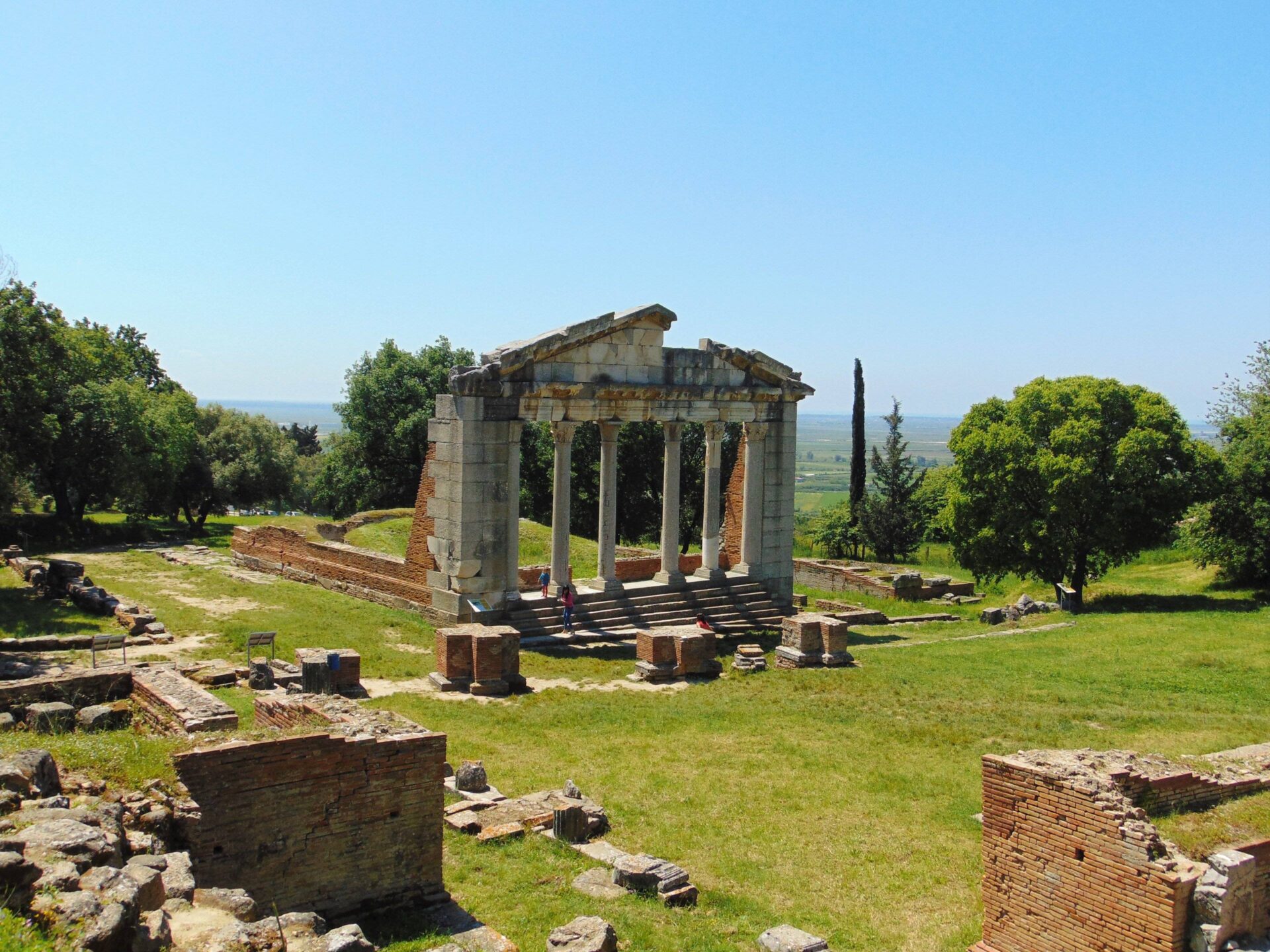 Panoramic view of an Albanian hillside town with stone-roofed houses and a historic fortress overlooking a valley under a soft off-season sky