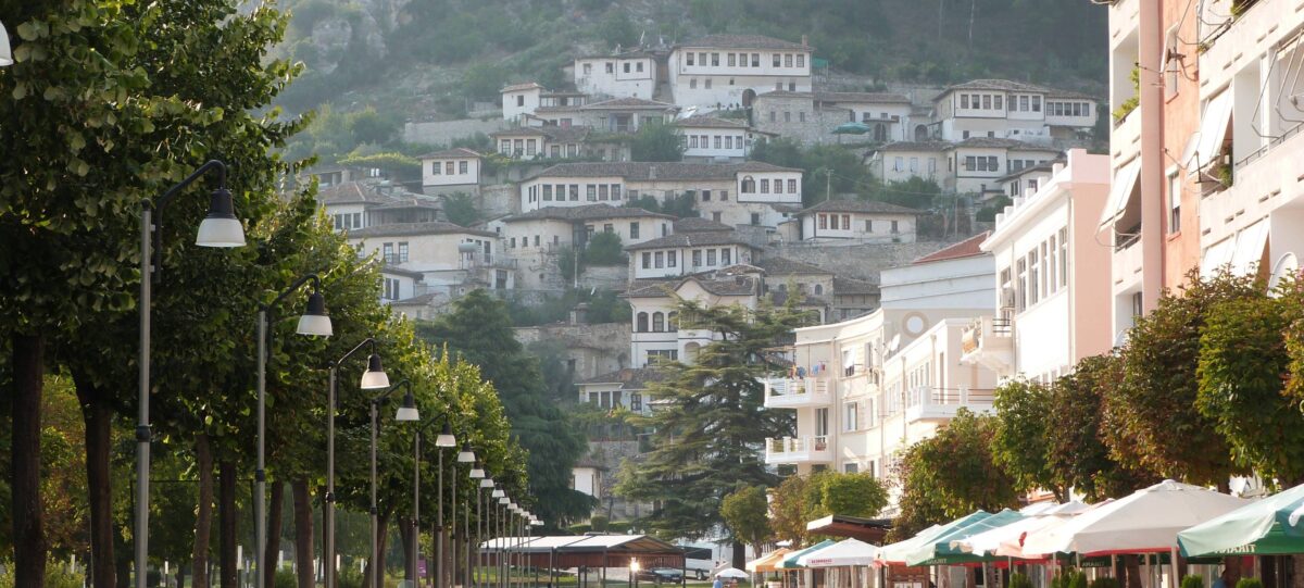 Panoramic view of Berat with white Ottoman houses stacked on a hillside, many windows facing the river and fortress above