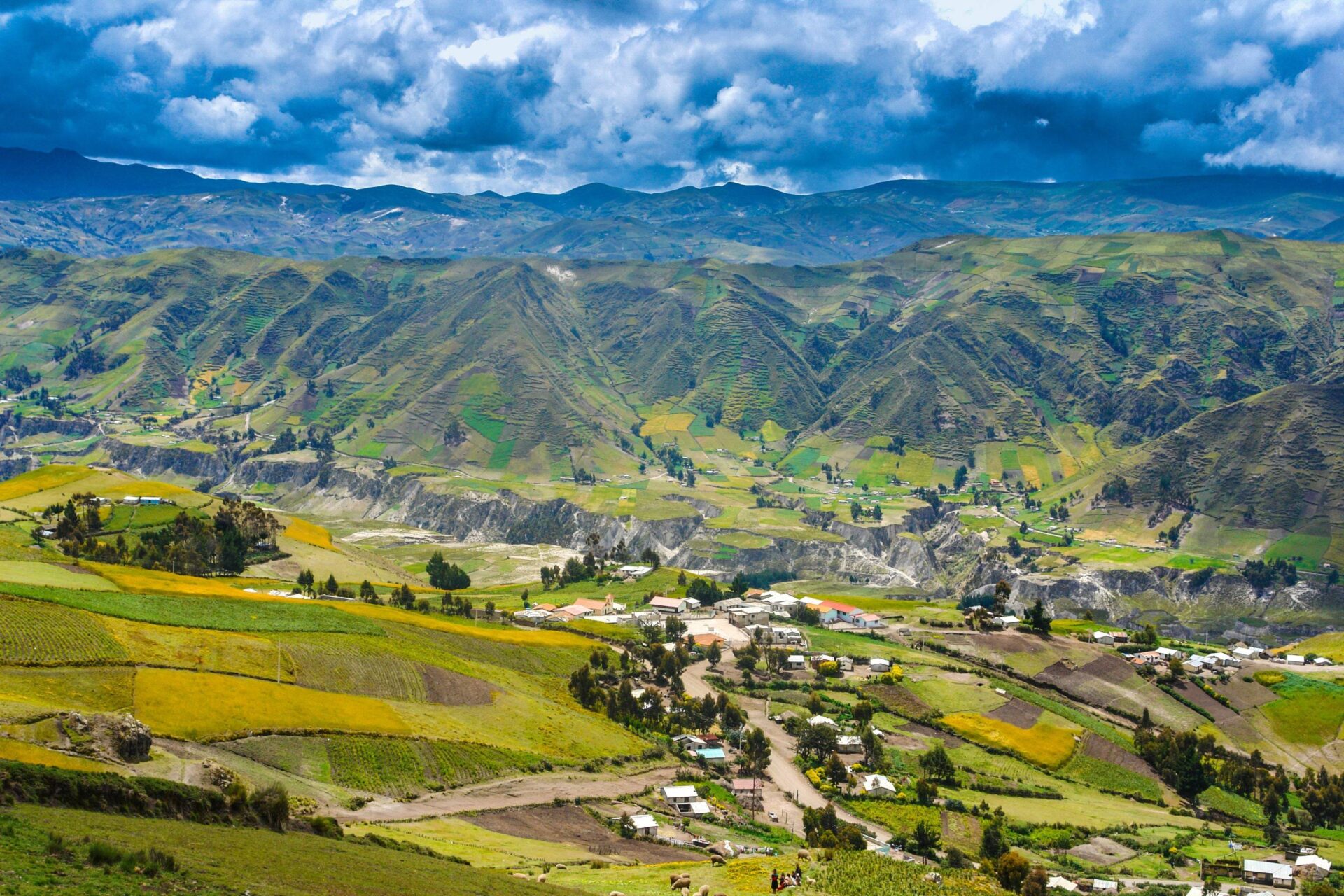 Panoramic view of the Ecuadorian Andes with a snow-capped volcano rising above green valleys under a clear blue sky