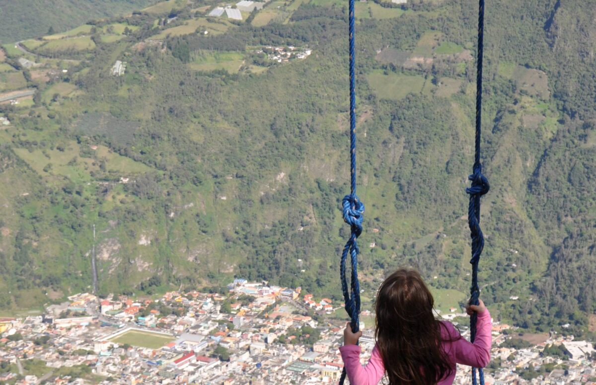 Panoramic view over Baños with surrounding green mountains and a swing overlooking the valley