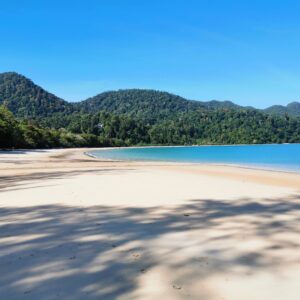 Panoramic tropical beach scene on Langkawi Island with turquoise sea, white sand and lush green hills under a bright blue sky