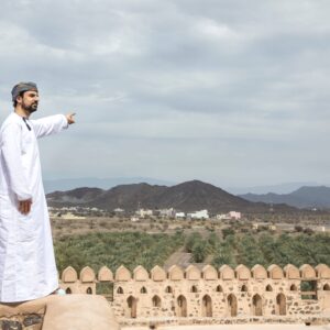 Golden sand dunes of the Wahiba Sands desert in Oman at sunset with 4x4 tracks and distant camp tents under a clear sky