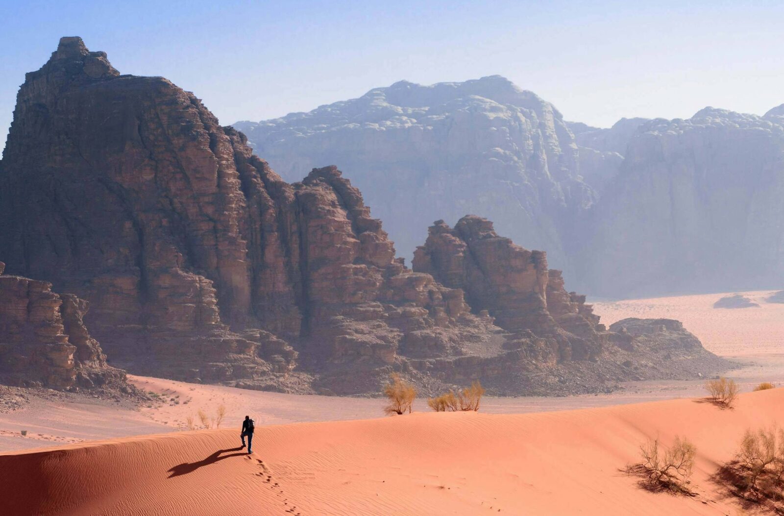 Camel caravan crossing the red sand dunes of Wadi Rum with towering rock formations in the background