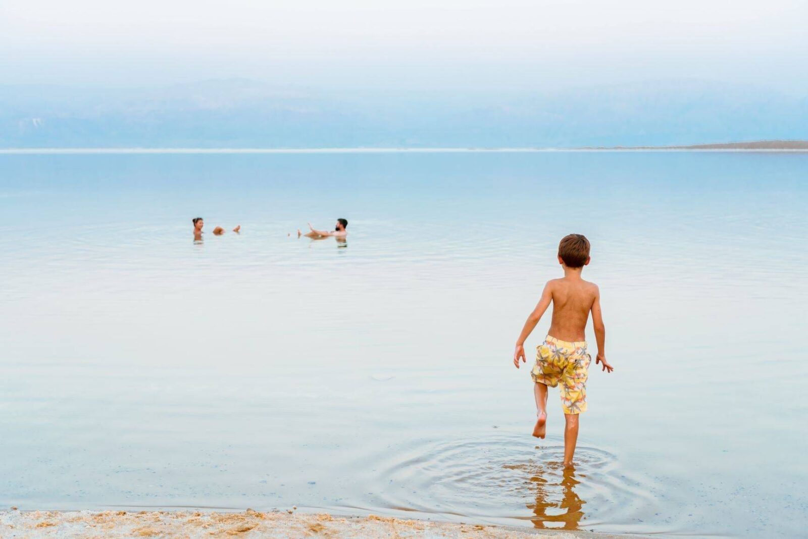 Person floating effortlessly on the calm waters of the Dead Sea with mountains in the distance