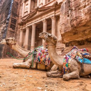 Group of travelers walking through the sandstone canyon Siq towards the Treasury in Petra, Jordan, under a clear blue sky