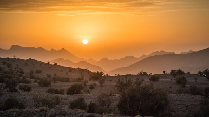 Panoramic view of Muscat with traditional white buildings, mosque domes and coastal mountains at sunset in Oman