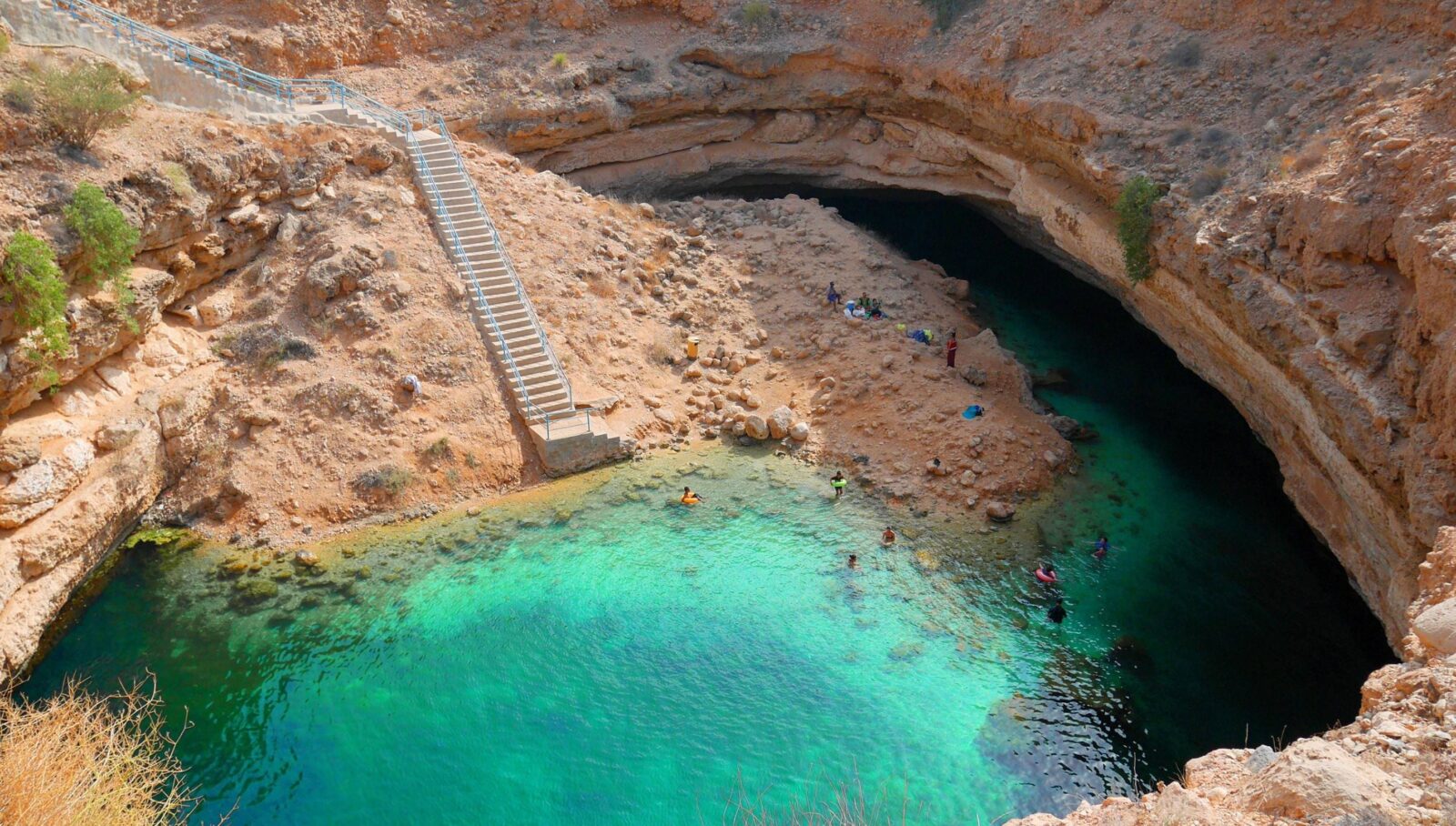 Turquoise inlet of Wadi Shab framed by steep cliffs and palm trees near the white-sand coast of Oman