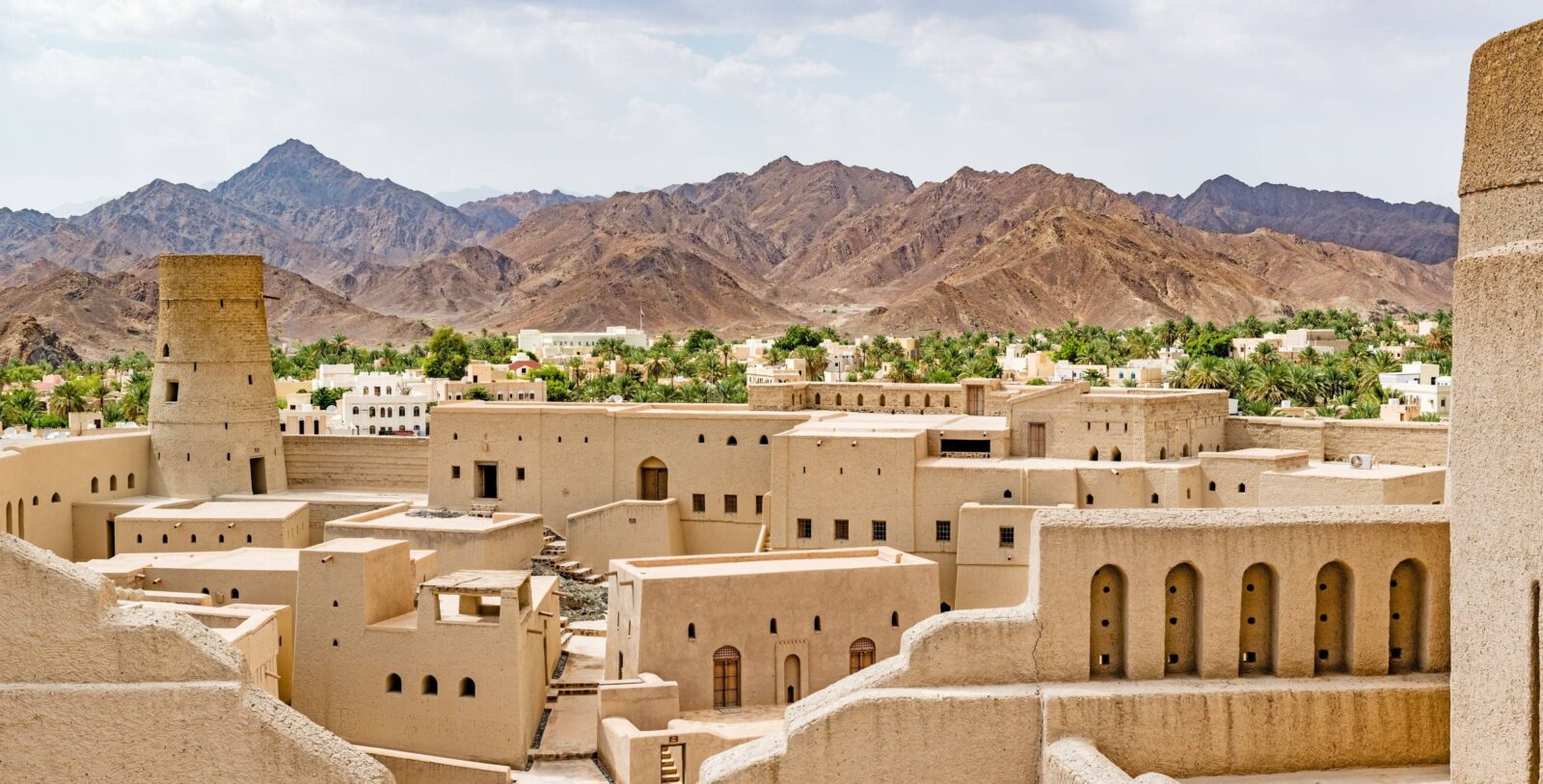 Historic Jabrin Castle in Oman with sand-coloured walls, towers and palm trees under a clear blue sky