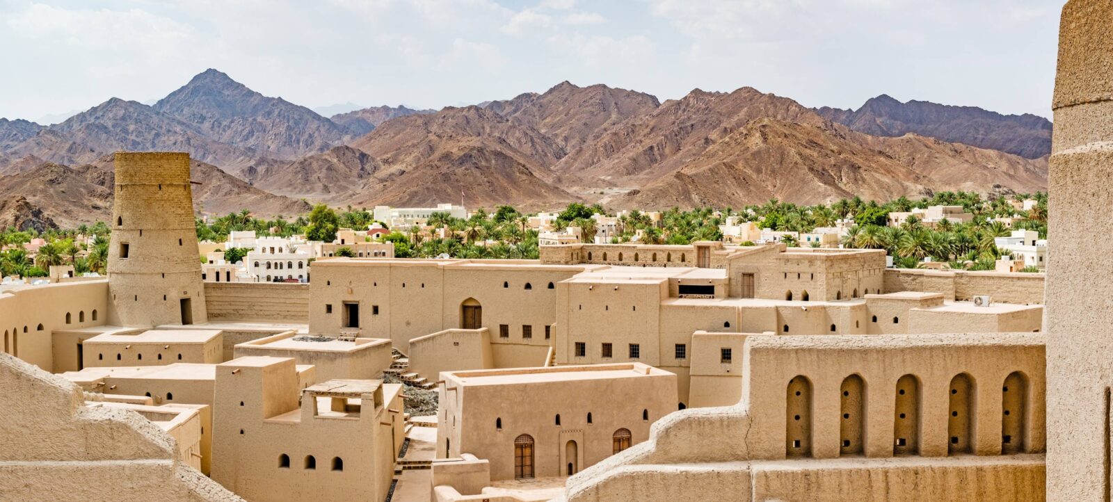 View of Nizwa Fort and surrounding palm oasis with mountains in the distance