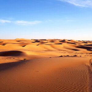 Panoramic view of Oman’s rugged mountains and desert landscape under a clear blue sky, showcasing winding roads and rocky peaks
