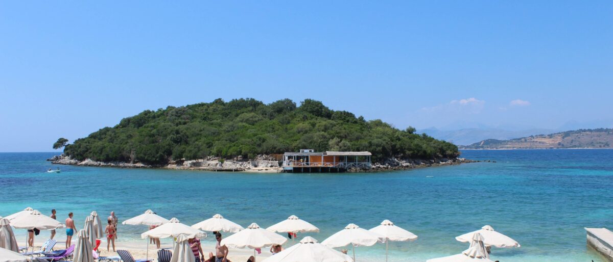 Scenic stretch of the Albanian Riviera with winding coastal road, turquoise Ionian Sea and green hills dropping steeply to the shore