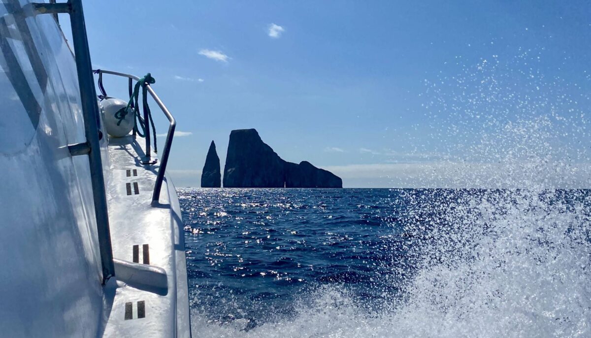Sheer rock walls of Kicker Rock rising from the ocean with a snorkel boat nearby