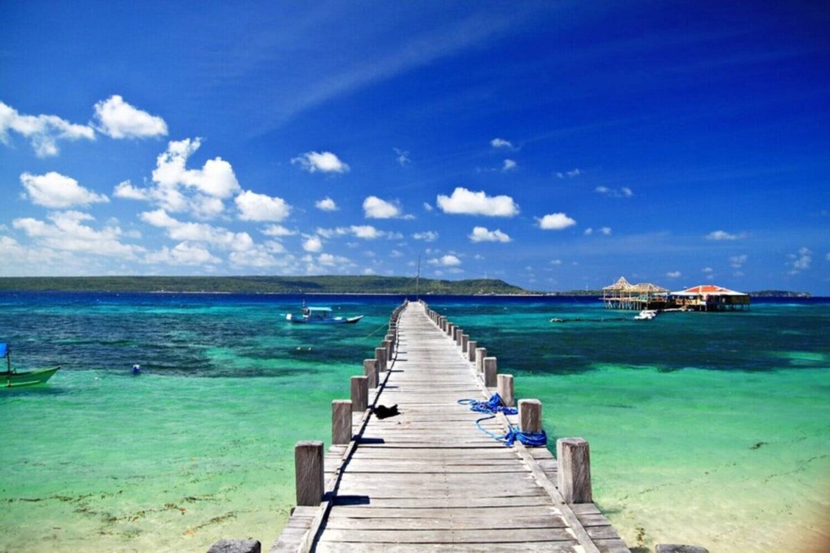 Small boat near Liukang Loe island with people snorkeling above coral reef and a white sand beach behind