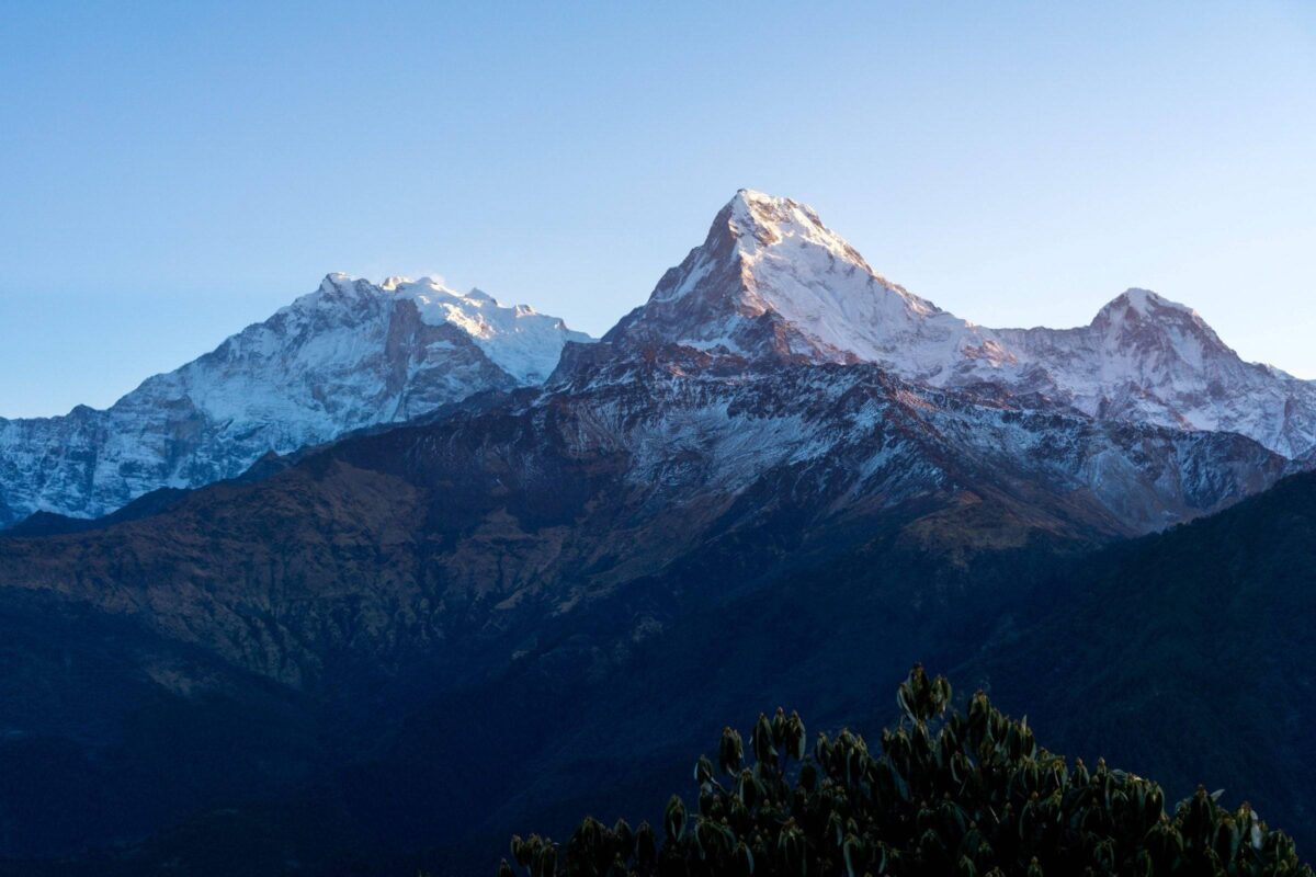 Sunrise view from Poon Hill with trekkers silhouetted against orange sky and a panorama of snow-covered Himalayan peaks