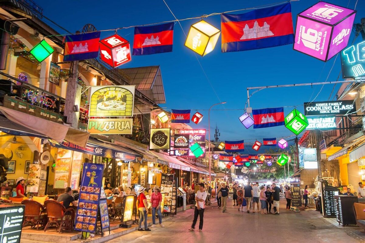 Tourists walking among ancient stone ruins and trees in the Angkor temple area near Siem Reap, Cambodia