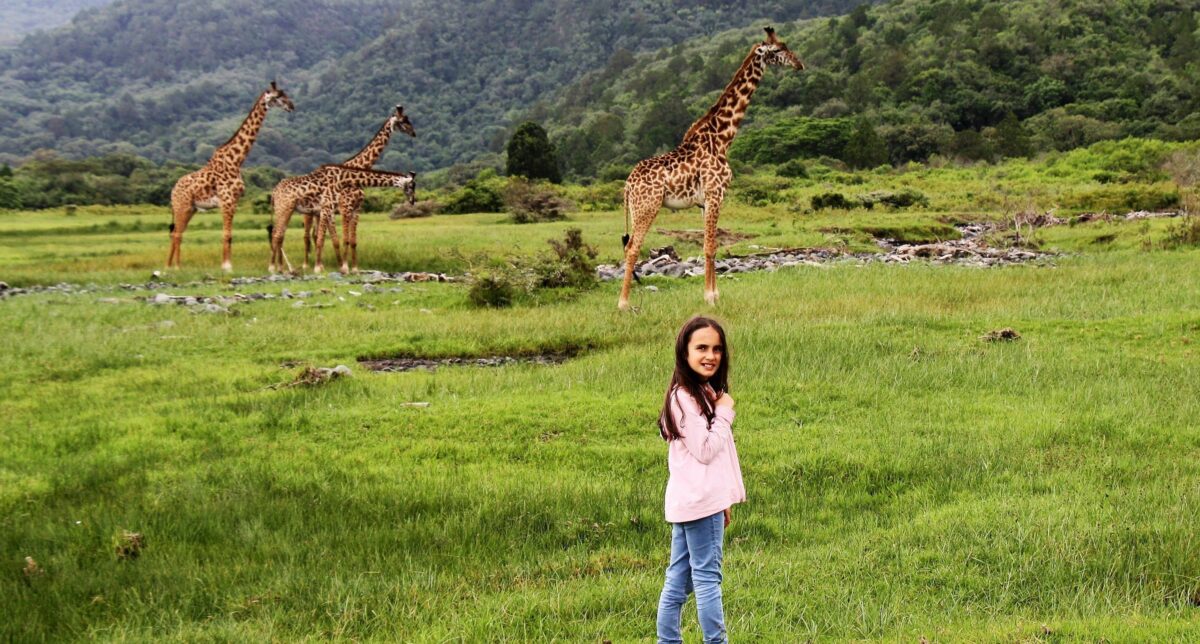 Tourists walking with a park ranger in Arusha National Park surrounded by green forest and grazing giraffes